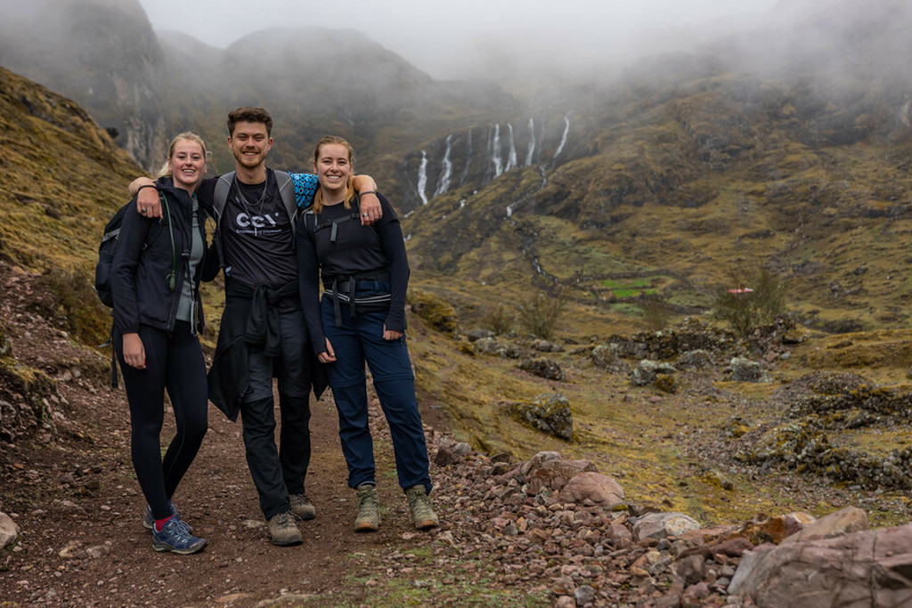 22-35ers groepsrondreis Peru: drie reizigers wandelen door de Andes met watervallen op de achtergrond.