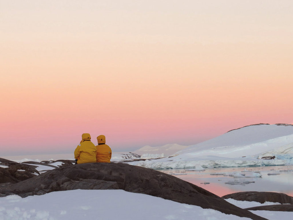 Reizigers in gele jassen kijken uit over het Antarctische ijslandschap bij zonsondergang tijdens de groepsrondreis.