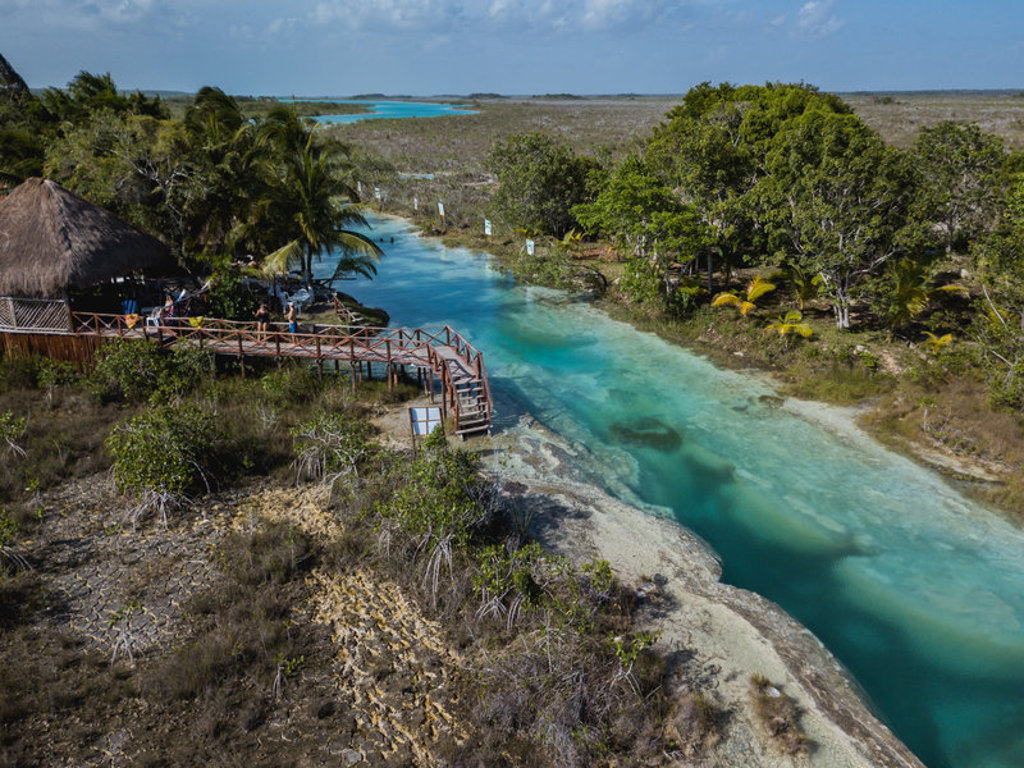 Houten wandelpad langs een turquoise lagune met palmbomen in Mexico, tijdens een 22-35ers groepsrondreis.