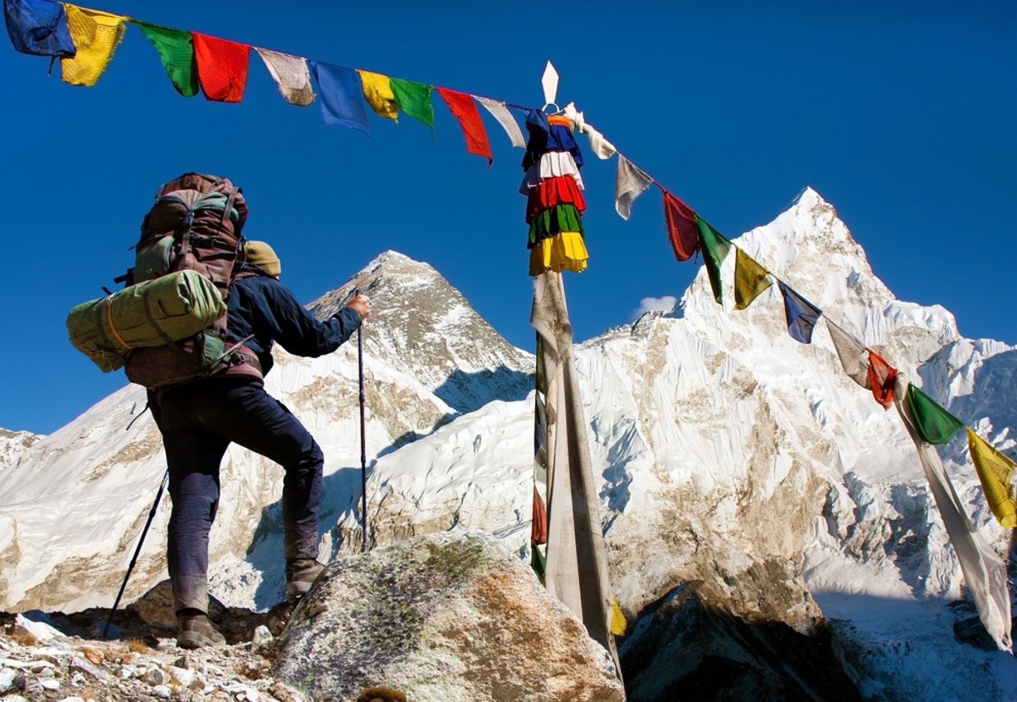 Trekker met rugzak bij gebedsvlaggen in de Himalaya, met besneeuwde bergtoppen in Nepal.