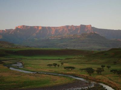 Groene vallei met kronkelende rivier en bergmassief bij zonsondergang in Zuid-Afrika.