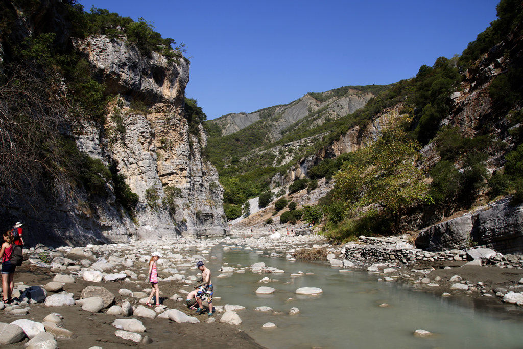 Kinderen spelen in een rivierbedding tussen hoge rotswanden tijdens een familiereis in Albanië.