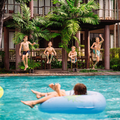 Kinderen springen in het zwembad bij een tropisch resort tijdens een familiereis Thailand.