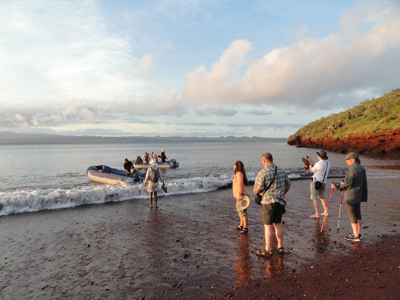 Reizigers stappen uit een zodiac op een rood zandstrand op de Galapagoseilanden tijdens de route Galapagoseilanden.