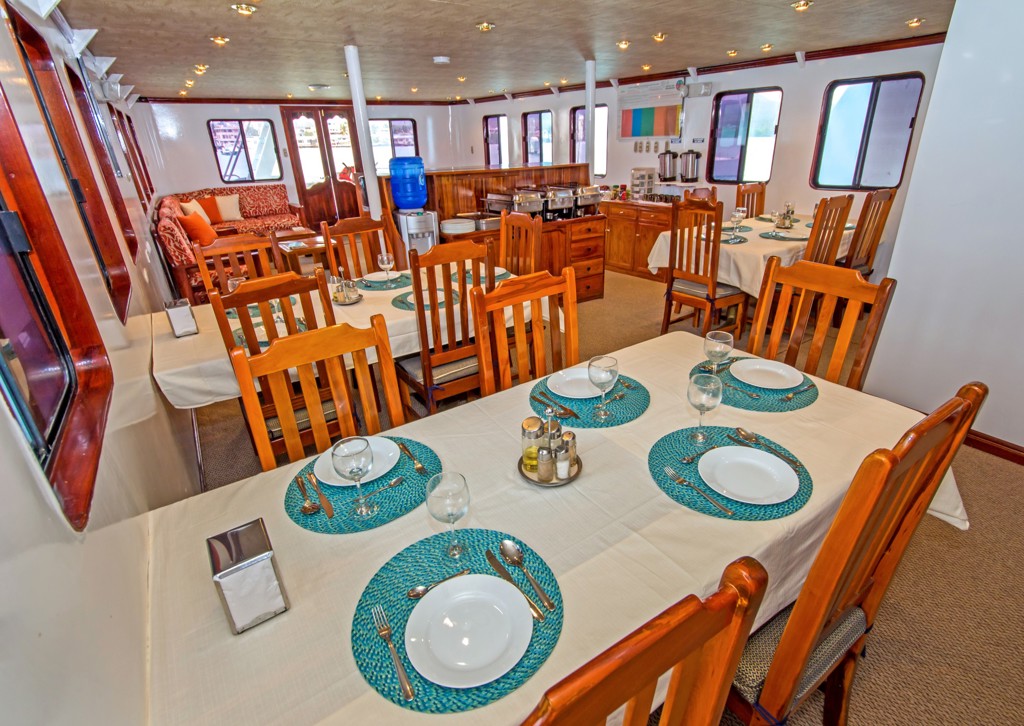 Eetzaal aan boord van een cruiseschip tijdens groepsrondreis Galapagoseilanden, met gedekte tafels en houten stoelen.