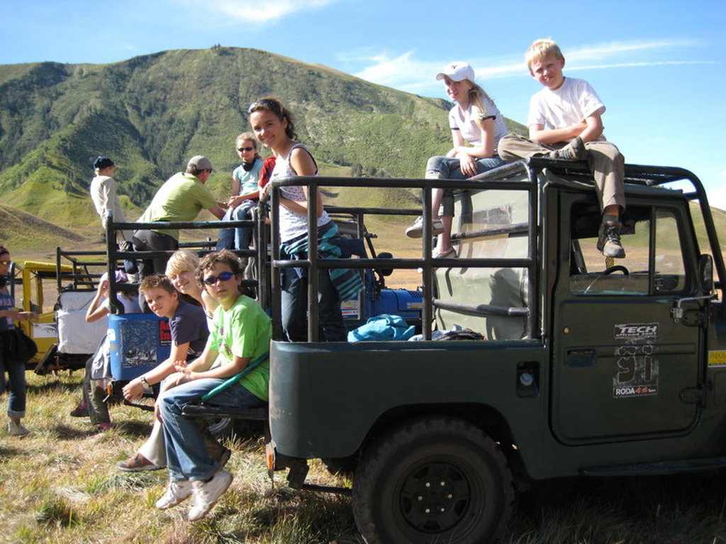 Gezin in open jeep tijdens safari in nationaal park op Sumatra, met groene bergen op de achtergrond.