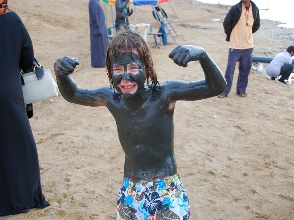 Kind bedekt met zwarte modder aan de Dode Zee in Jordanië tijdens een familiereis.