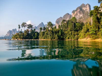 Karstbergen en groene jungle langs een helder meer in Thailand, met weerspiegeling in het water.