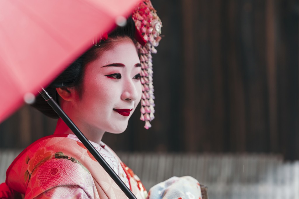 Japanse geisha in kimono met rode paraplu, sfeerbeeld voor familiereis Japan.