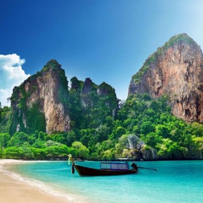 Longtailboot voor een strand met kalkstenen kliffen en turquoise zee in Thailand.
