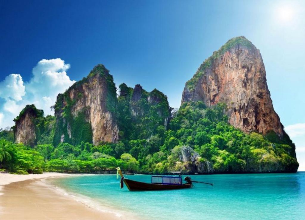 Longtailboot voor een strand met kalkstenen kliffen en turquoise zee in Thailand.