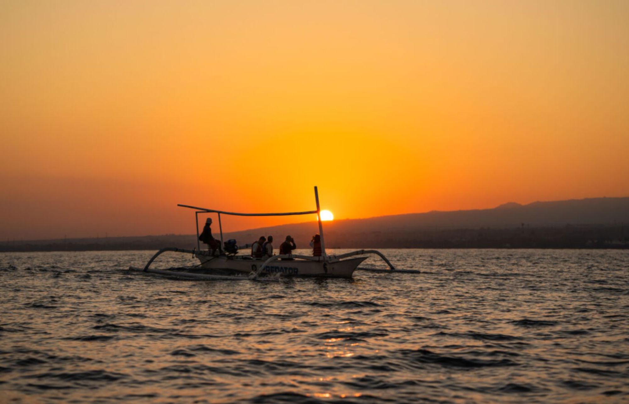 Traditionele outriggerboot met passagiers bij zonsondergang op zee in Indonesië.