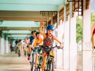 Kinderen fietsen met helm door een overdekte gang tijdens de Route Thailand.