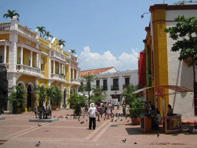 Gezellig plein in Cartagena met kleurrijke gevels, palmbomen en mensen tussen duiven tijdens Route Colombia.