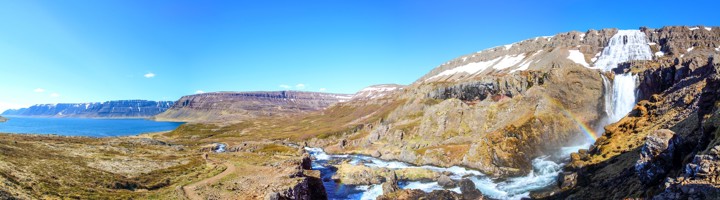 Dynjandi-waterval in de Westfjorden van IJsland, met rivier, bergen en regenboog boven het water.