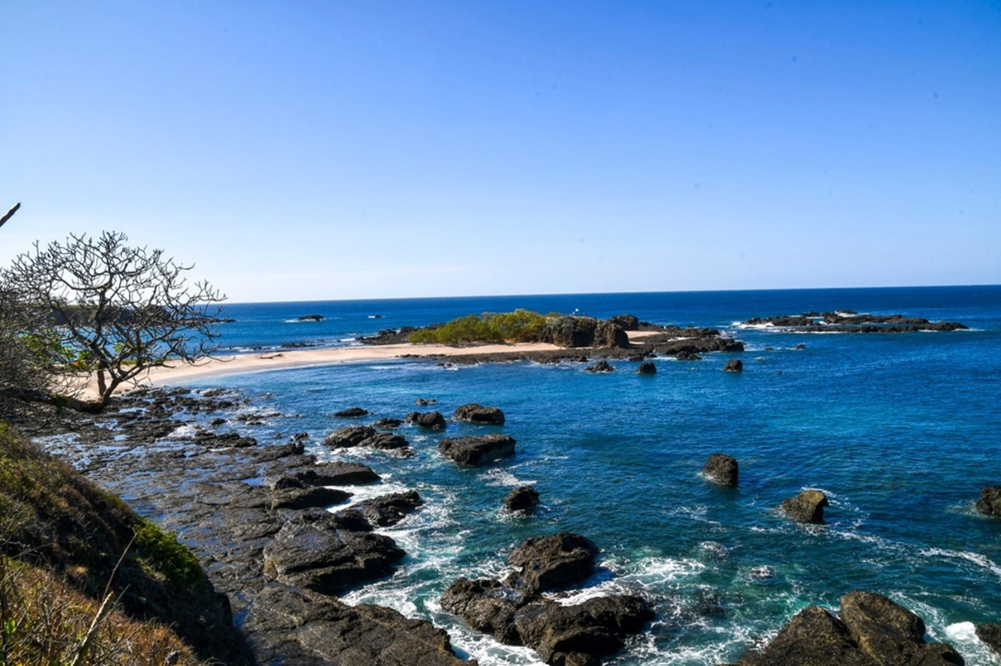 Rotsachtige kust met zandstrand en helderblauw zeewater in Costa Rica.
