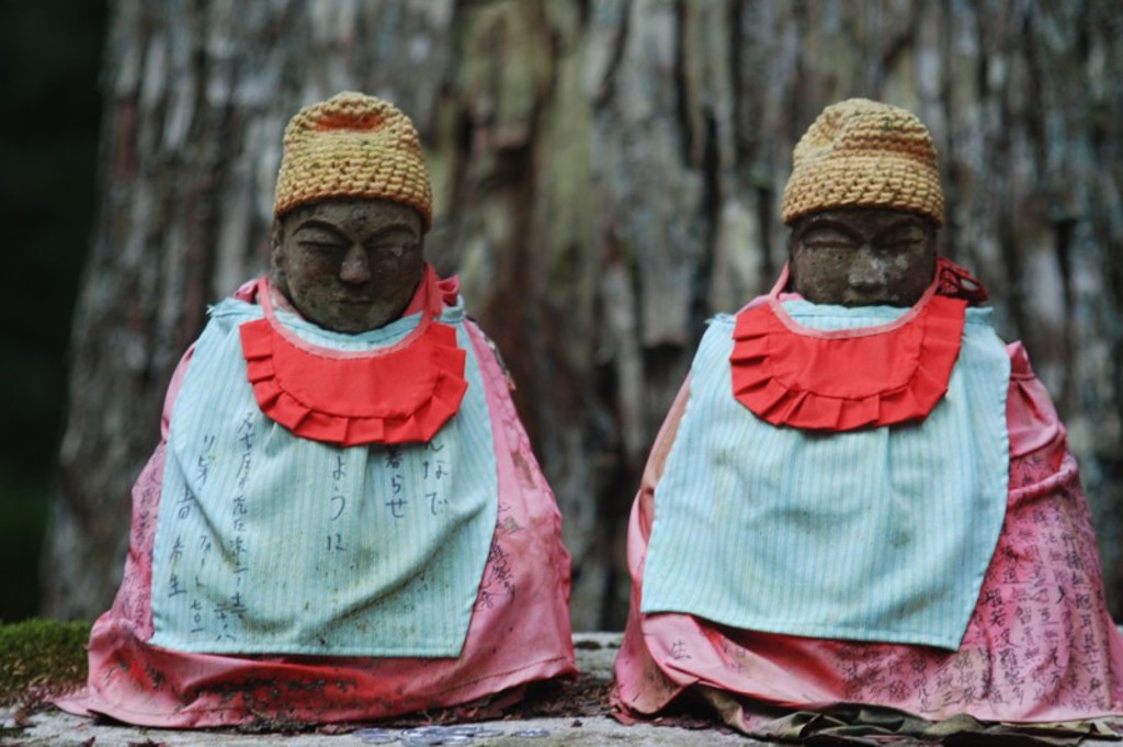 Twee Jizo-beeldjes met rode slabbetjes en gebreide mutsen in een Japanse tempeltuin tijdens groepsrondreis Japan.