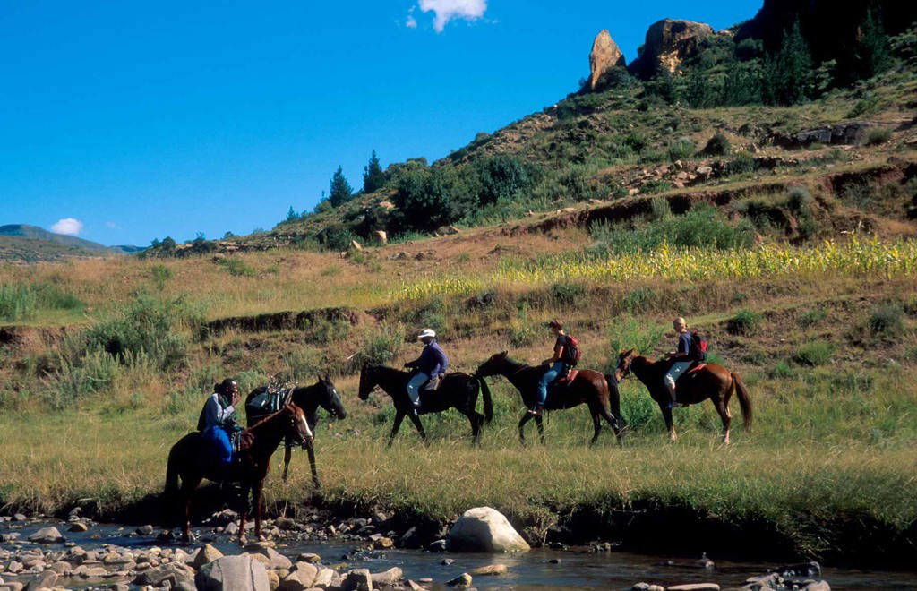 Ruiters te paard steken een rivier over in de bergen van Lesotho tijdens een groepsrondreis Zuid-Afrika, eSwatini en Lesotho.