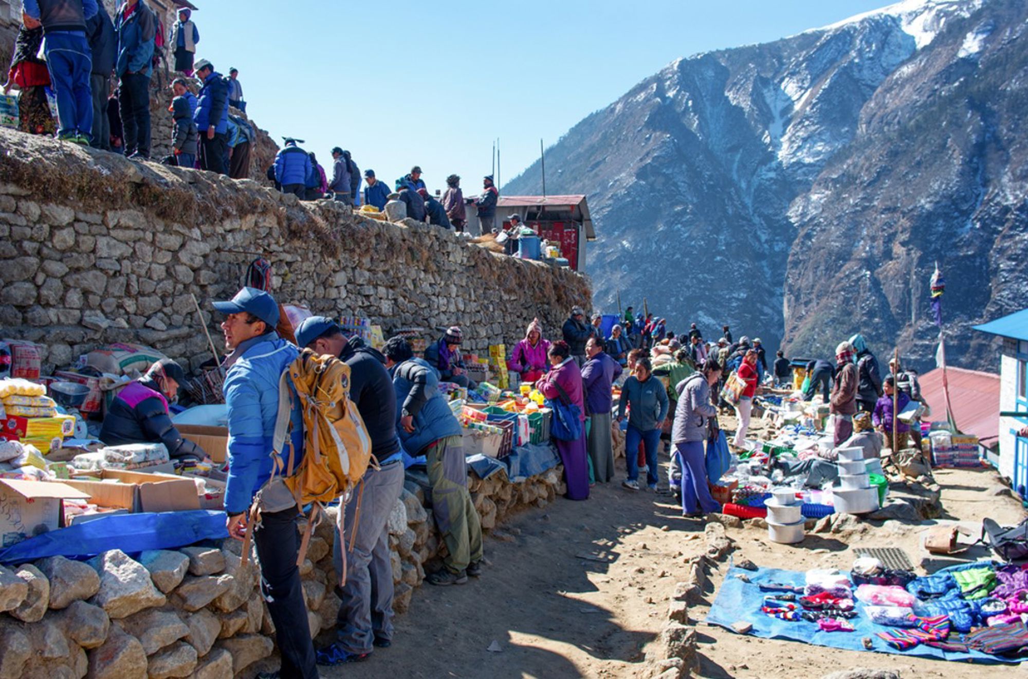 Drukke bergmarkt met wandelaars en kraampjes langs een stenen muur in de Himalaya, Nepal.
