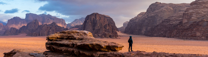 Reiziger in de Wadi Rum-woestijn in Jordanië, met rotsformaties en bergen bij zonsondergang.