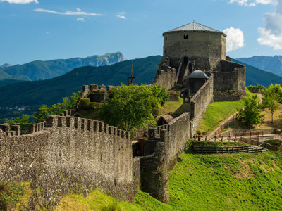 Middeleeuws kasteel op een groene heuvel in Toscane, met berglandschap op de achtergrond.