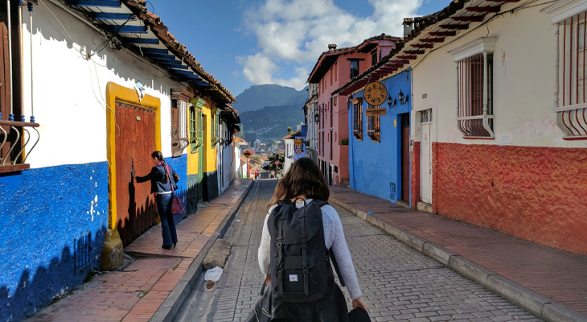 Backpacker loopt door kleurrijke straat in Bogotá, Colombia, met bergen op de achtergrond.
