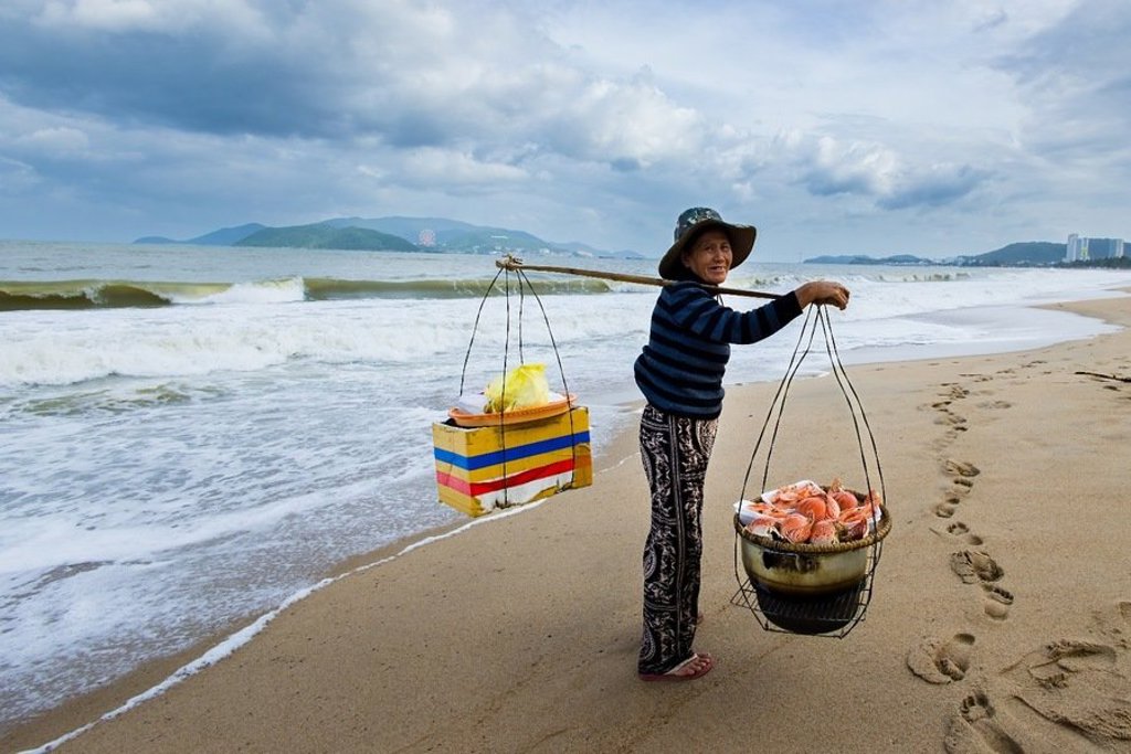 Vietnamese vrouw met traditionele draagstok en manden langs het water tijdens een fietsvakantie in Vietnam.