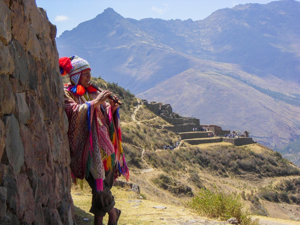 Muzikant in traditionele kleding speelt fluit bij de Inca-ruïnes van Pisac in de Heilige Vallei, Peru.
