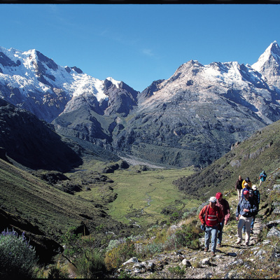 Wandelaars op de Takesi Trail met uitzicht op besneeuwde bergtoppen en een groene vallei.