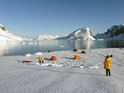 Kampeerplek met tenten op het ijs aan een rustige baai met ijsbergen en besneeuwde bergen, Route Antarctica.