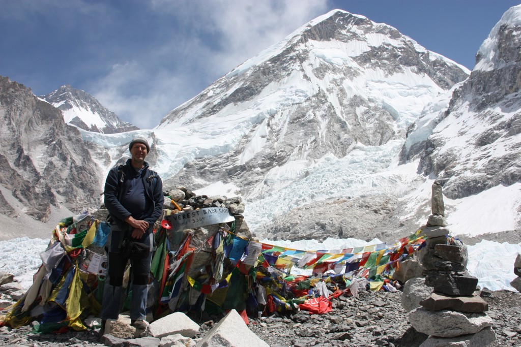 Wandelaar bij Everest Base Camp in Nepal, met gebedsvlaggen en besneeuwde bergtoppen op de achtergrond.