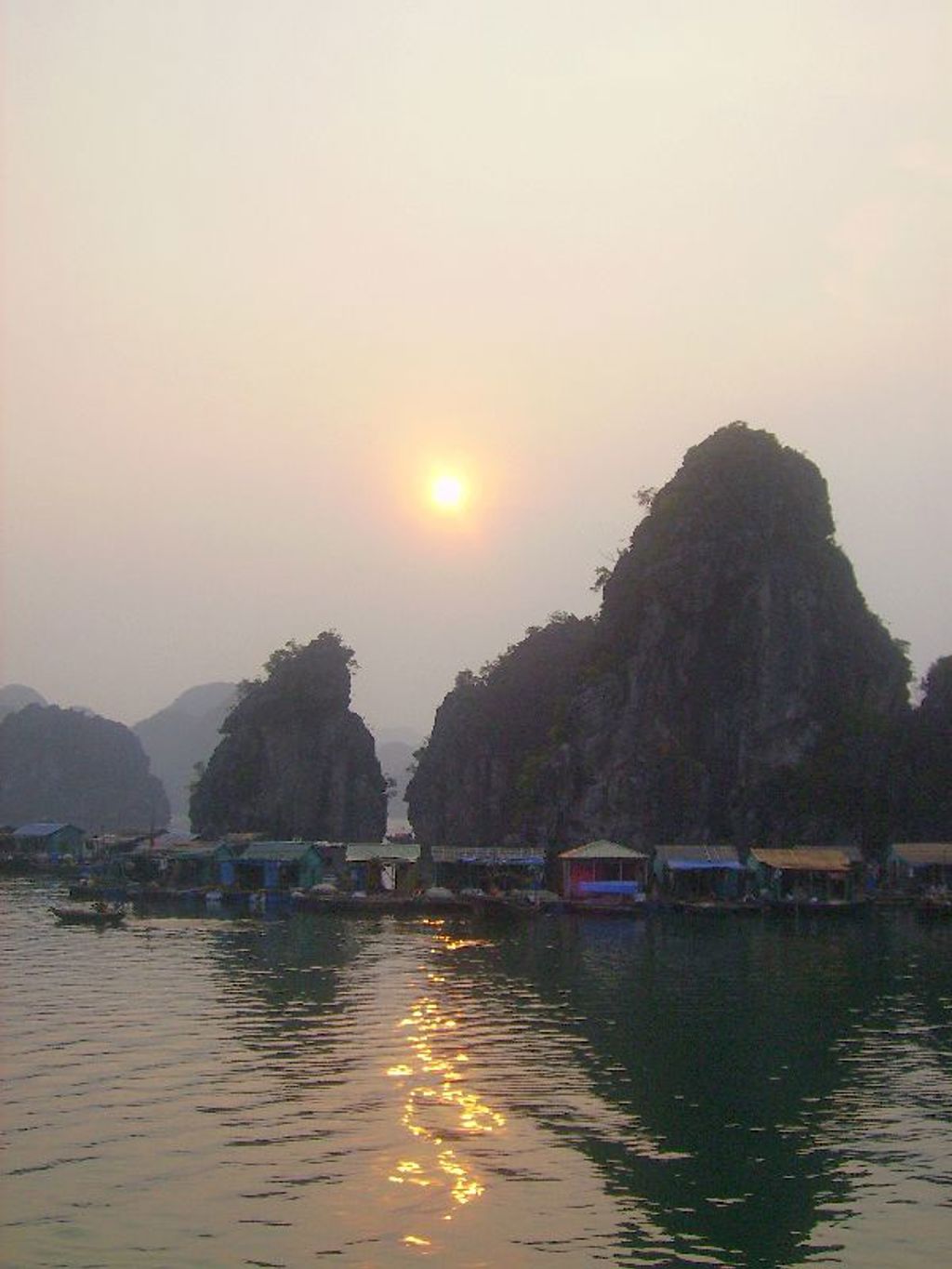 Zonsondergang boven Halong Bay met kalksteenrotsen en drijvende vissersdorpjes in Vietnam.