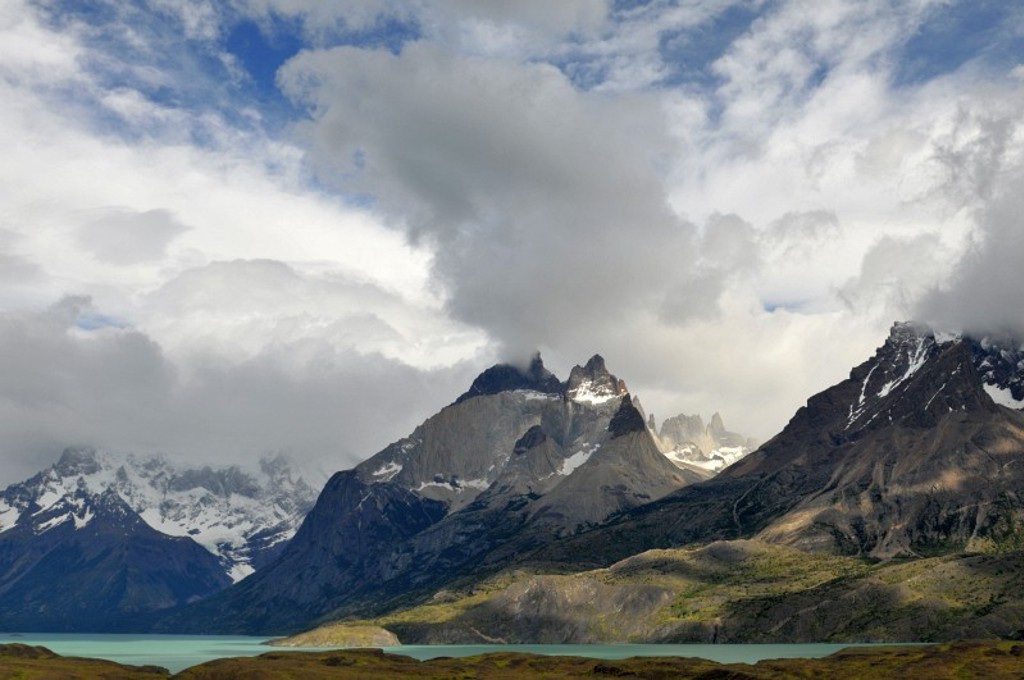 Azuurblauw meer met besneeuwde bergtoppen in Patagonië onder dramatische wolkenlucht.