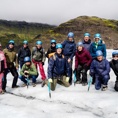 Groep wandelaars met helmen en ijsbijlen tijdens een gletsjerwandeling, met bergen op de achtergrond.