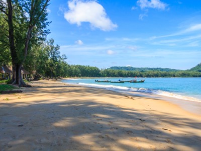 Rustig zandstrand met palmbomen en longtailboten voor de kust in Thailand.