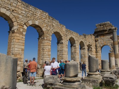 Groepsreis Route Marokko: bezoekers bij de Romeinse ruïnes van Volubilis met stenen bogen en zuilen.