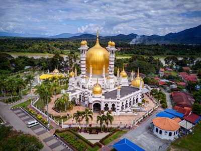 de Ubudiah-moskee in Kuala Kangsar met gouden koepels, omringd door groen en bergen.