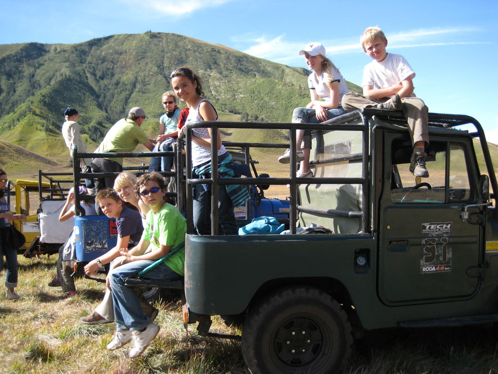 Gezin en kinderen in een open jeep tijdens een familiereis op Java en Bali, met groene bergen op de achtergrond.