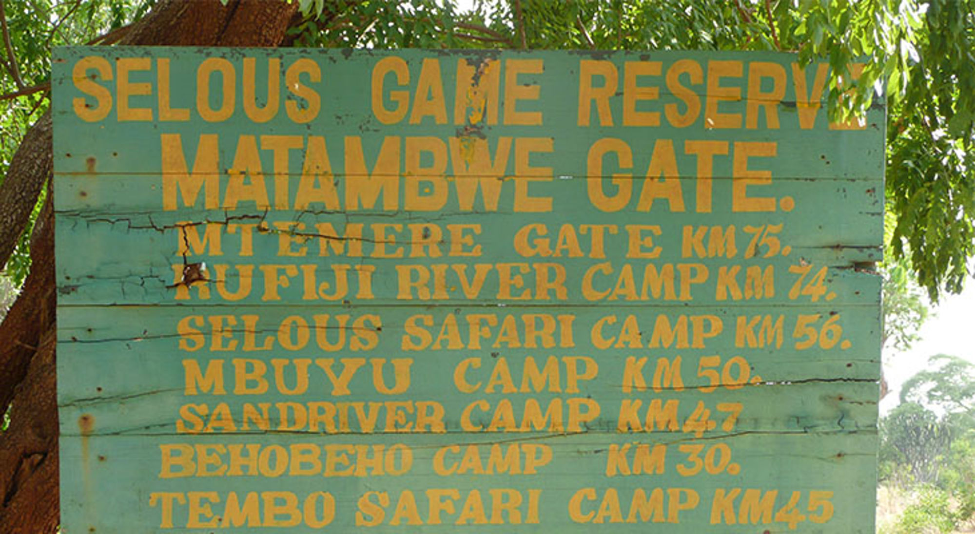 Matambwe Gate bord bij Selous Game Reserve Houten wegwijzer bij Selous Game Reserve, Tanzania, met afstanden naar Matambwe Gate en safari camps.