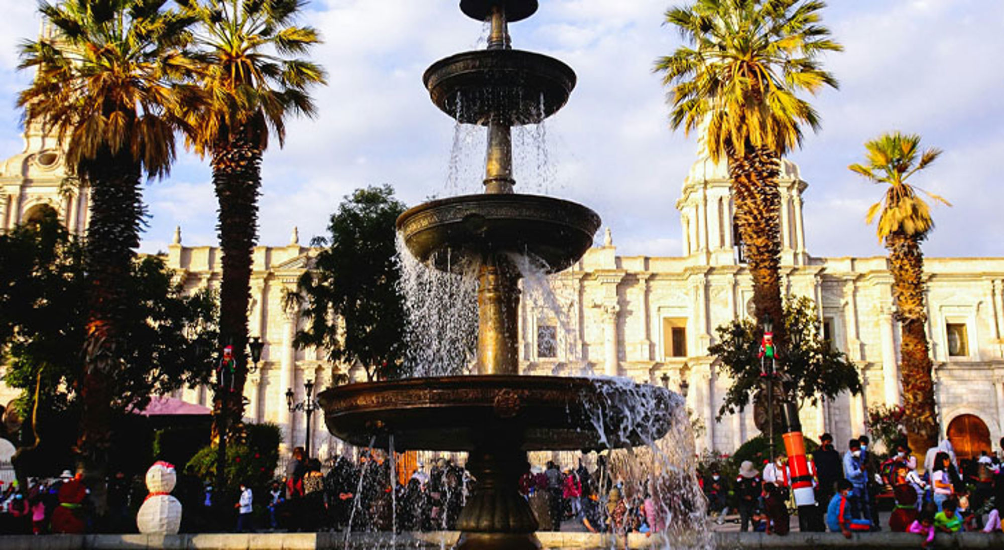 Arequipa Fontein op Plaza de Armas in Arequipa, met palmbomen en de kathedraal op de achtergrond.