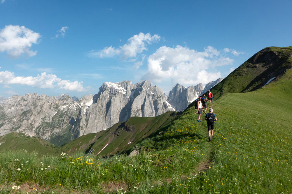 Wandelaars op bergpad met uitzicht op de Peaks of the Balkan, met ruige toppen en groene alpenweiden.