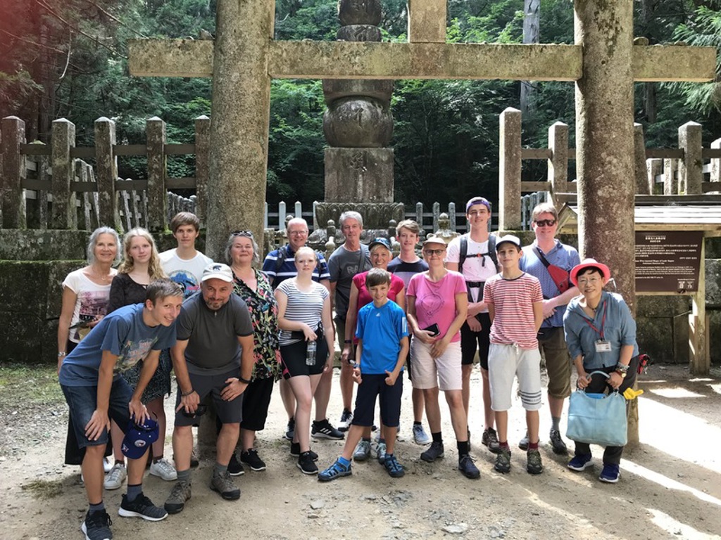 Groep reizigers tijdens een familiereis Japan bij een stenen torii-poort in een bosrijk tempelcomplex.