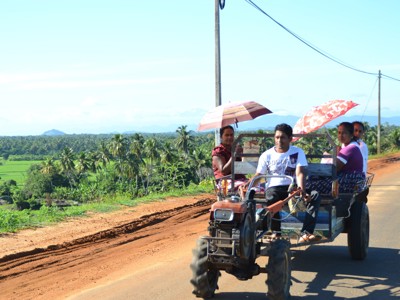 Tractor met aanhanger en passagiers op de weg langs rijstvelden en palmbomen in Sri Lanka.