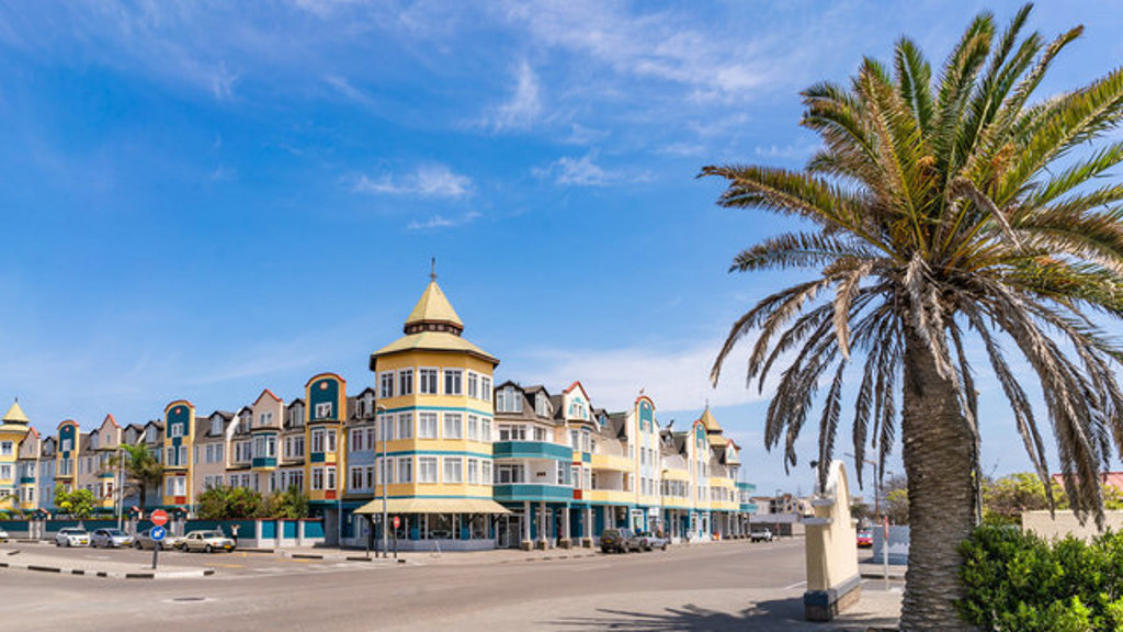 Pastelkleurige gevels aan de boulevard van Swakopmund, Namibië, met palmboom onder een blauwe lucht.