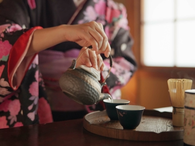 Japanse theeceremonie: persoon in kimono schenkt thee uit in kopjes, met matcha-klopper op een dienblad.