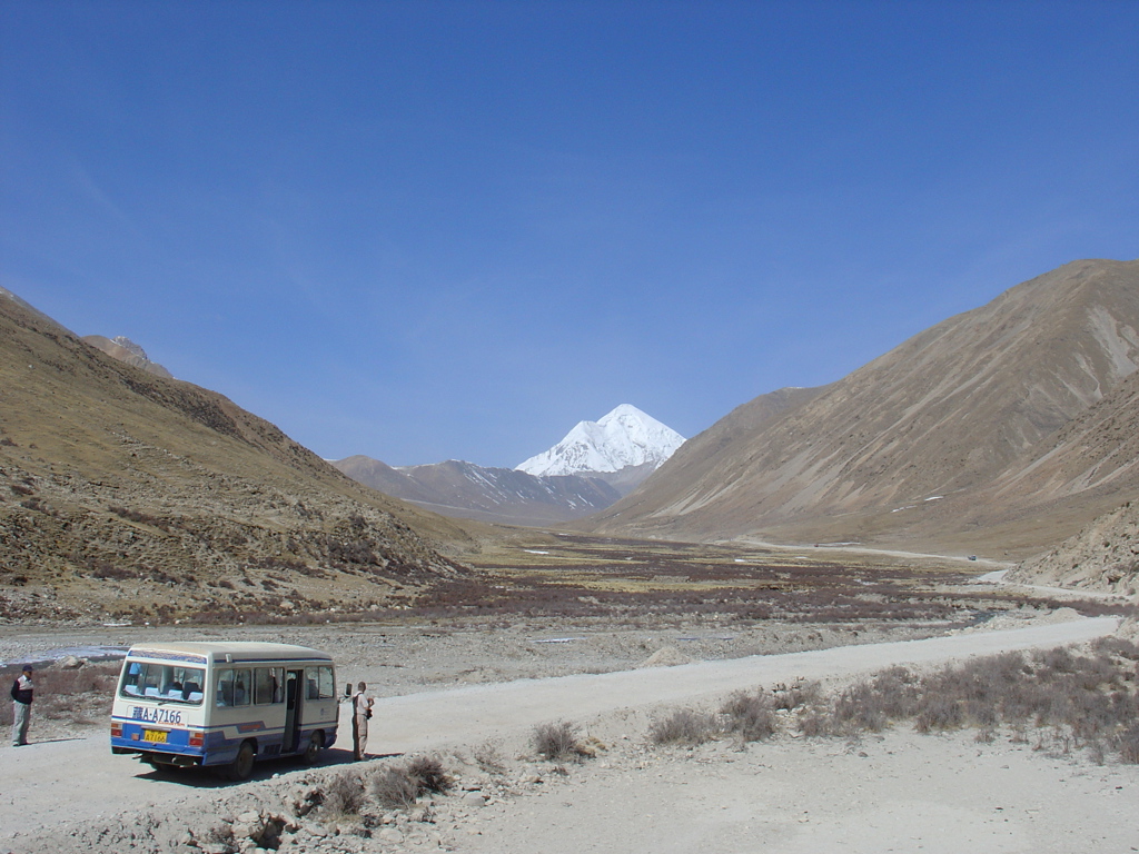 Bus in berglandschap met besneeuwde Himalaya-top tijdens groepsrondreis Tibet en Nepal.