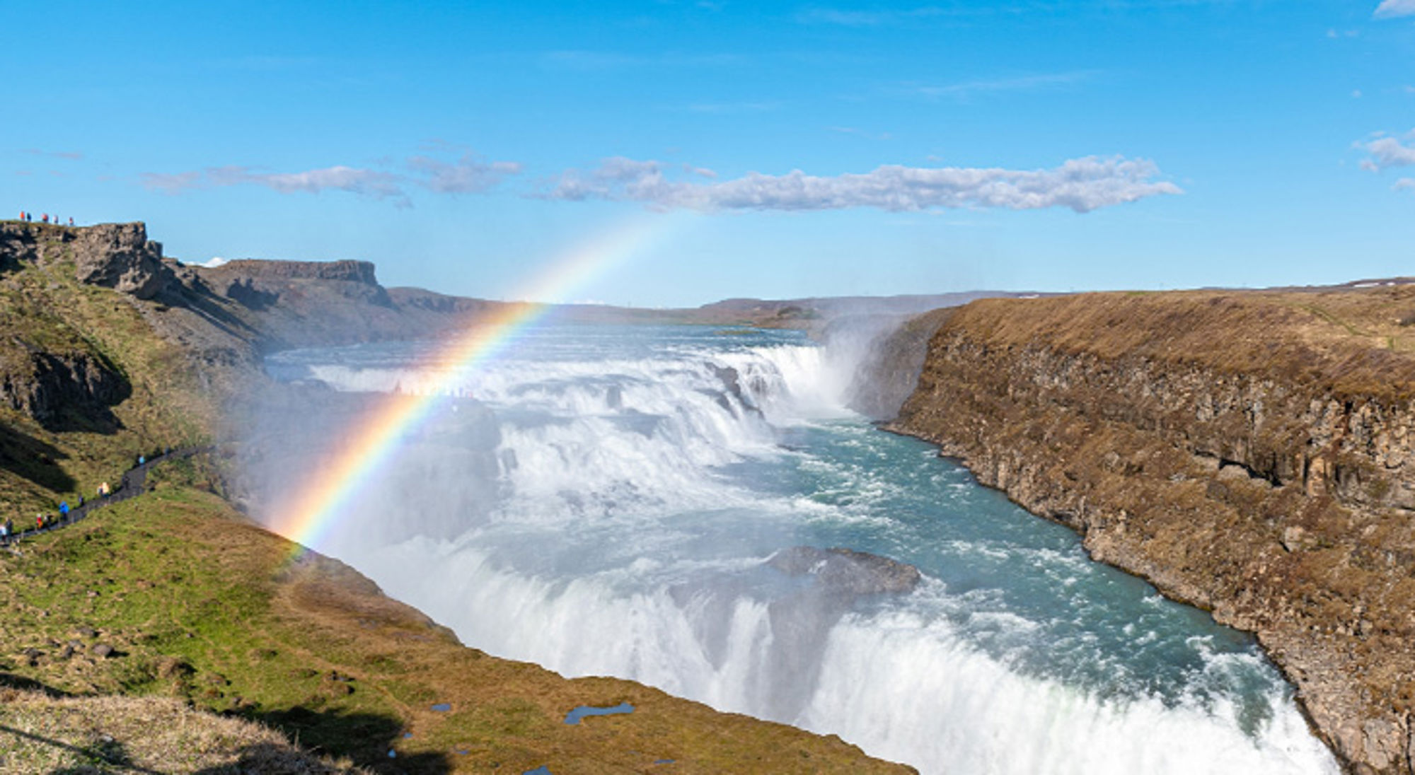 Gullfoss-waterval in IJsland met regenboog boven de kloof en kolkend rivierwater.