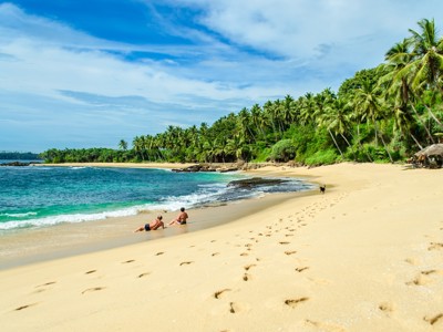 Tropisch zandstrand in Sri Lanka met palmbomen, turquoise zee en reizigers aan de waterlijn.