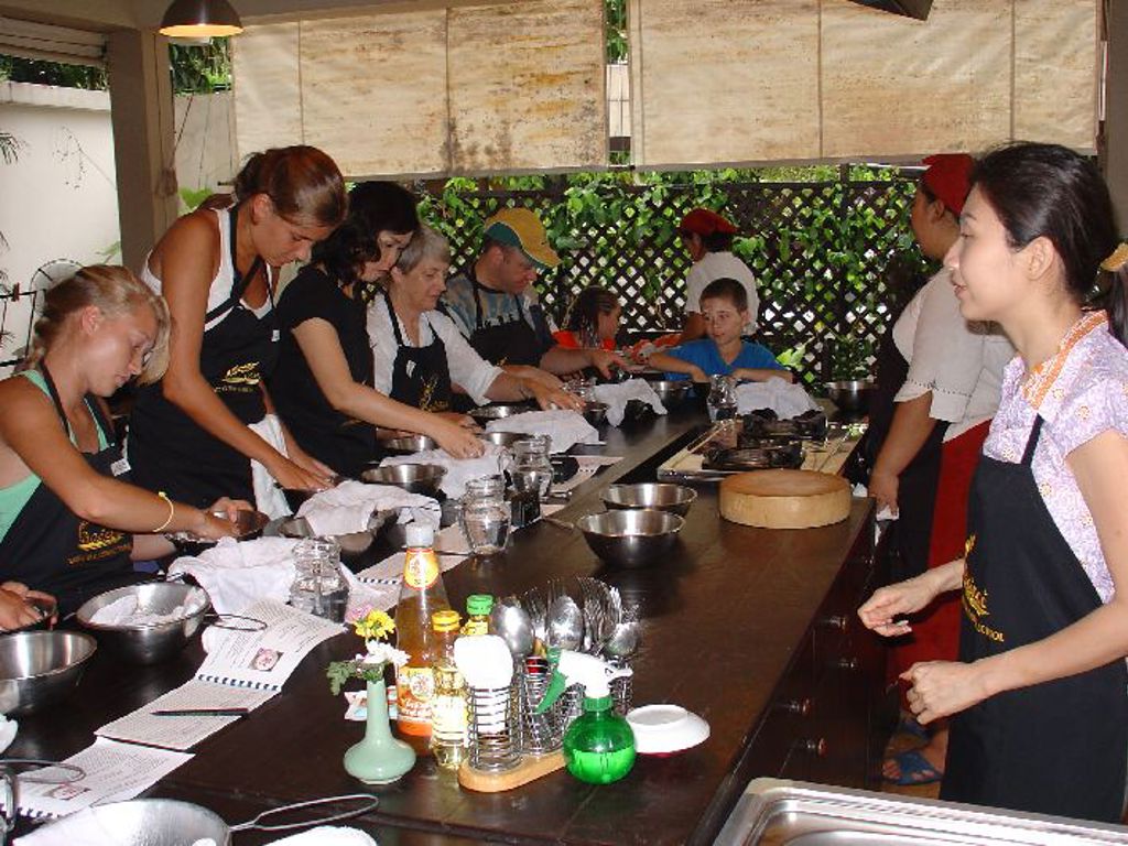 Kookworkshop tijdens familiereis Thailand, deelnemers bereiden samen Thaise gerechten aan een lange werktafel.