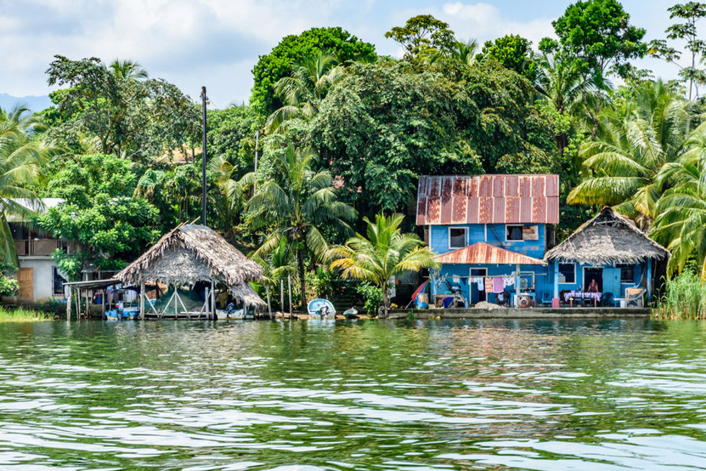 Kleurrijke huizen aan het water, omringd door tropisch groen in Guatemala tijdens een groepsrondreis naar Copán.